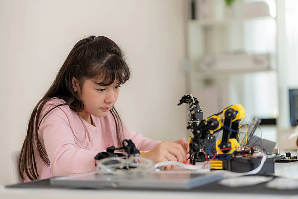 In a classroom equipped with robotics tools, a young girl uses a remote control to guide a robotic arm. The moment captures the essence of hands-on learning in STEM fields, fostering curiosity and skills in robotics, coding, and technology