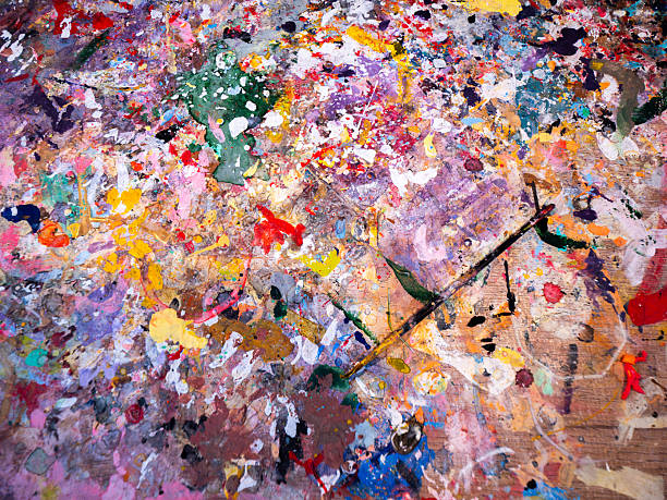 A close-up shot of a vibrant, paint-splattered palette with a cleverly hidden paintbrush. It evokes creativity and inspiration in art making. Ideal for use as a background or element in designs that require vibrancy and creative flair