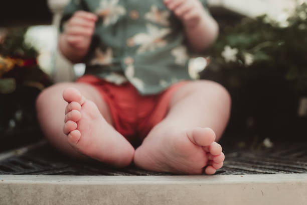 Little baby toddler boy sitting outdoors with bare feet and toes