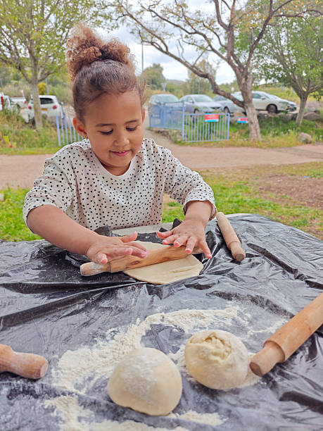 Girl Rolling Dough into Flatbread at Outdoor Table.