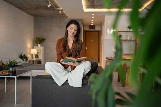 istock Young woman reading a book on sofa in modern apartment 2206845701