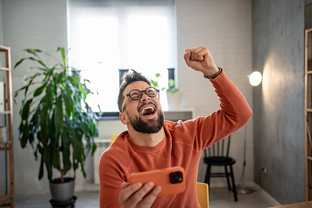istock Excited man celebrating success while holding smartphone at home 2206852081