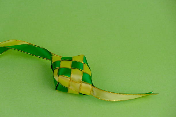 istock hand crafted ketupat or rice dumpling packaging from ribbon isolated on green background. Ramadan and Hari Raya Eid al-Fitr decoration for template, card, and background 2206859514