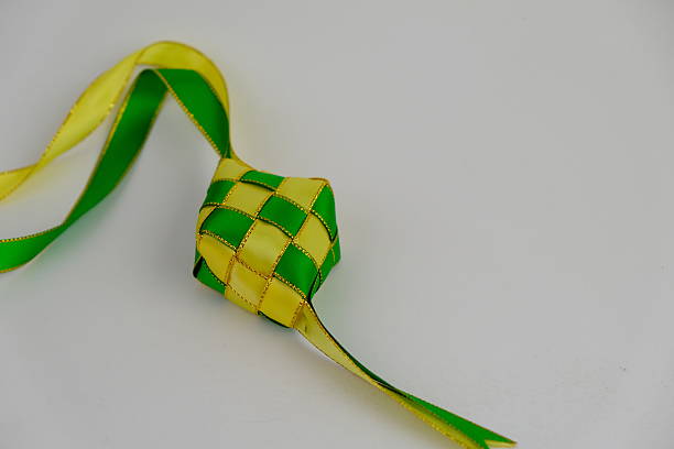 istock hand crafted ketupat or rice dumpling packaging from ribbon isolated on green background. Ramadan and Hari Raya Eid al-Fitr decoration for template, card, and background 2206859553