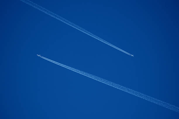 Looking up at a pair commercial passenger jets flying at a high altitude with their vapor trails intersecting against the blue sky. Concept - Crowed skies