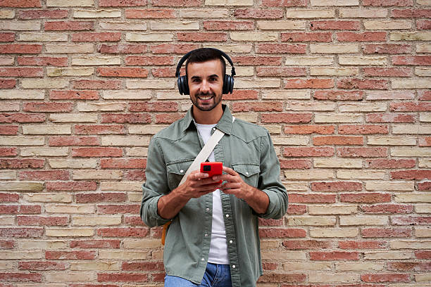 istock Caucasian man looking at camera smiling while using phone to send online messages and listen music. 2206864627