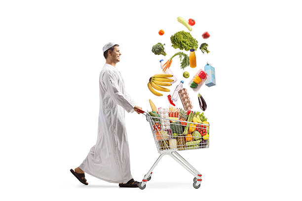 Middle eastern man pushing a shopping cart with falling food assortment isolated on white background