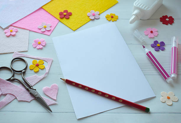 istock Creative flat lay composition of DIY greeting card crafting materials, including colorful felt flowers, scissors, glue, and blank paper, arranged on a white wooden background, showcasing the process of making a personalized handmade card 2206868845