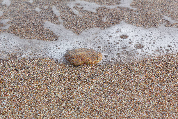 One stone on the sand on the seashore with sea foam