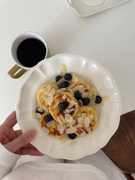 Enjoy a delightful breakfast of fluffy pancakes topped with fresh blueberries and crunchy almonds on white plate holding by woman.
