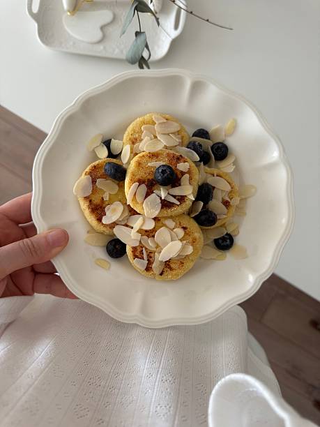Enjoy a delightful breakfast of fluffy pancakes topped with fresh blueberries and crunchy almonds on white plate holding by woman.