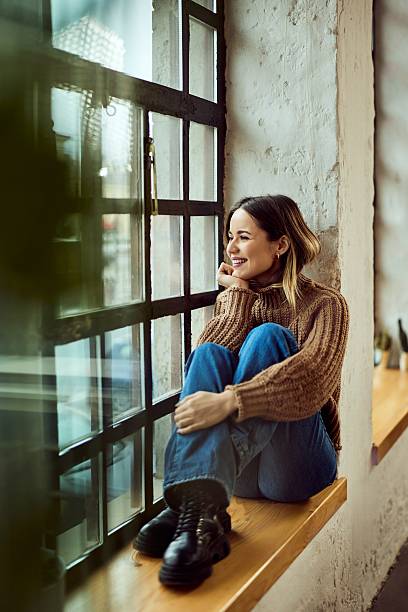 istock Smiling Woman Sitting by Window Reflecting in Urban Interior Setting 2206871070