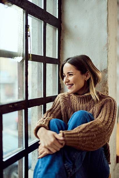 istock Young Woman Relaxing by a Window in Cozy Sweater Smiling Peacefully 2206871076