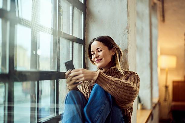 istock Smiling Woman Using Smartphone Next to a Window in a Stylish Interior 2206871079