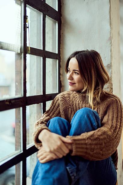 Woman Sitting by a Window in Comfortable Attire Reflecting Peacefully