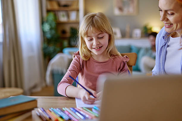 istock Smiling girl drawing with colored pencils and using a laptop with her mother 2206876556