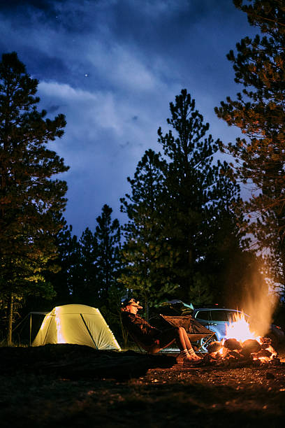 Woman car camping with tent in forest enjoys campfire at sunset, Arizona