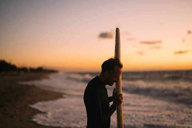 Photo of a male surfer at the beach, holding his surfboard