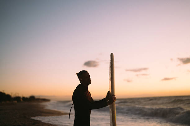 Photo of a male surfer at the beach, holding his surfboard