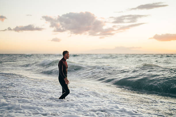 Photo of a male surfer at the beach, wearing a wetsuit, entering the ocean