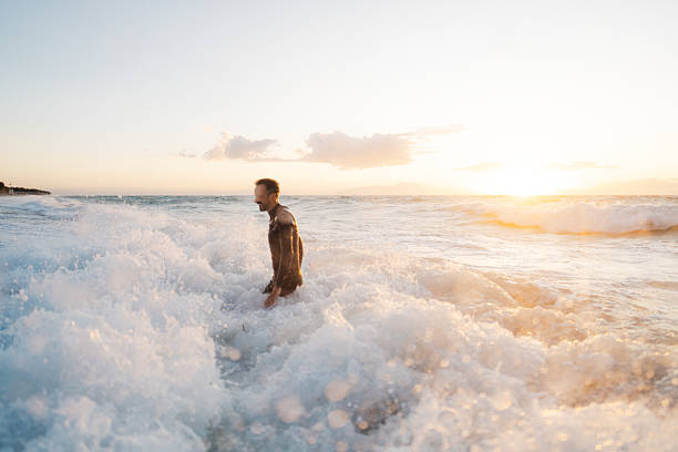 Photo of a male surfer at the beach, wearing a wetsuit, entering the ocean