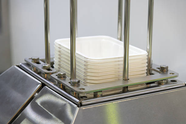 Stacked disposable containers rest on a metal platform, showcasing a modern industrial stacking machine in a busy manufacturing facility during daytime operations.