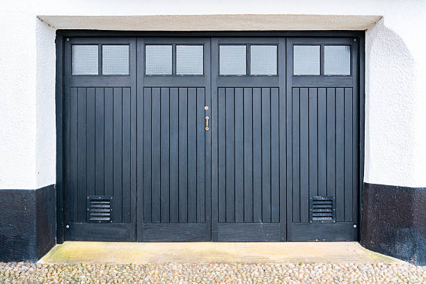 Grey closed garage door with windows and air vents, featuring a brass handle and pebble driveway