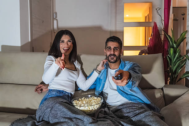 istock Couple watching tv and pointing at the screen while enjoying popcorn 2206882634