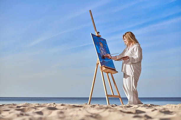 istock Young female artist painting on tranquil beach setting 2206887371