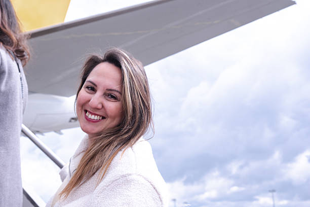 A middle-aged woman smiles at the camera as she boards a plane, filled with excitement for the journey ahead. A moment of adventure and new beginnings.