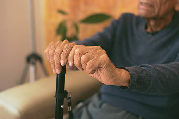 istock Elderly man holding walking stick while sitting on sofa at home: close-up of hands 2206894911
