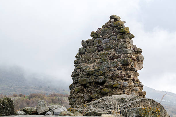 Weathered stone remains stand against misty backdrop in Crimea. Overcast sky creates moody atmosphere, highlighting structures aged texture. Gray tones and soft light enhance historic scene
