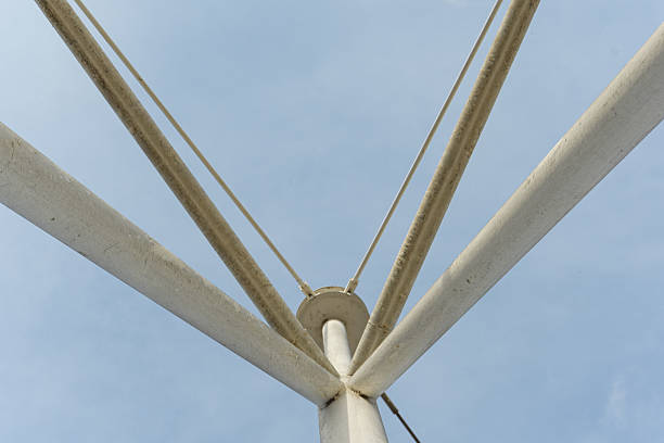 This close-up image focuses on the central connection point of a metal truss structure, highlighting the intricate geometry of the beams converging at a central node. The upward perspective emphasizes the structural integrity and design of the truss, set against a clear blue sky. This photograph is ideal for projects requiring detailed visuals of architectural elements, industrial design, or abstract representations of truss shapes and connections