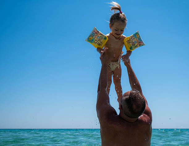 dad and daughter are playing in the sea, enjoying themselves, they are happy, the daughter is wearing a shirt