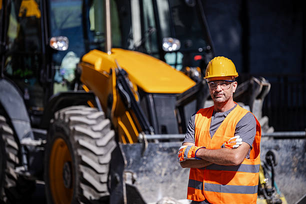 istock Construction worker stands confidently in front of a yellow excavator on a bright sunny day at a construction site 2206907760