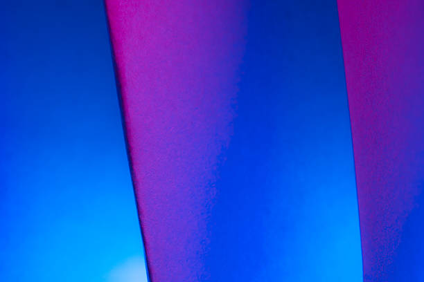 A striking arrangement of pink and blue paper forms two overlapping shapes. The artwork is illuminated by dramatic lighting.