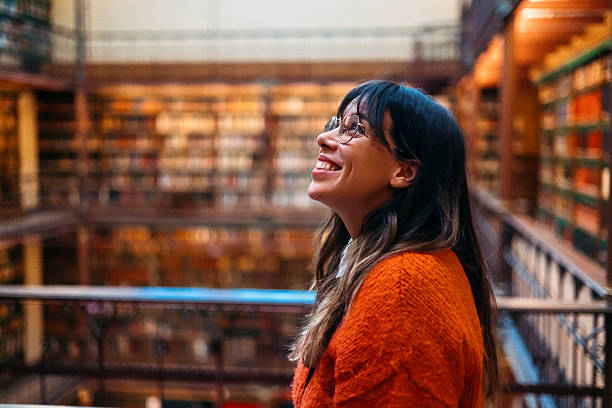 A cheerful young woman in an inviting library setting, radiating happiness and warmth. Surrounded by rows of books, this scene portrays a love for knowledge and a sense of contentment.