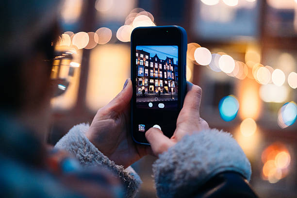A person photographing city buildings at night on their smartphone, featuring blurred bokeh lights in the background creating a vibrant and artistic ambiance.