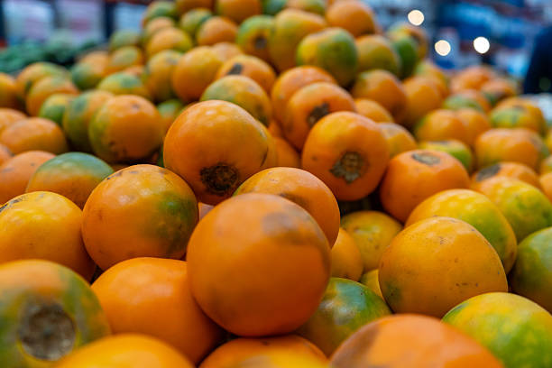 A large collection of fresh lulo fruits stacked at a local market. Their vibrant orange and green hues create a visually appealing texture, showcasing their exotic and tropical nature