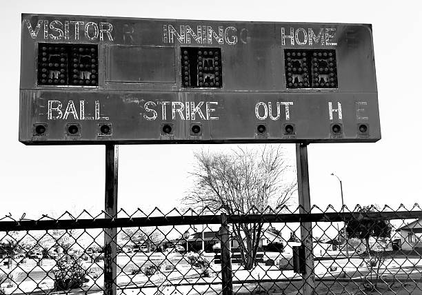 faded retro baseball scoreboard with chipped paint rusty metal vintage numbers cracked surface surrounded by weeds old lights above evoke nostalgia from decades of summer games and crowds cheering