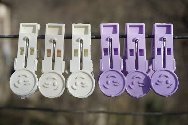 A colorful display of clothespins hanging on a clothesline, with three white clothespins and three in a soft lilac (light purple) shade. The gentle contrast between the colors creates a cheerful and organized scene, evoking a sense of simplicity and everyday life. The image captures the essence of outdoor chores, home life, and vibrant touches in everyday objects, making it ideal for themes related to home, laundry, and the beauty of small, functional details.