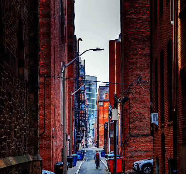 Boston, Massachusetts, USA - March 10, 2025:  View down a Public Alley in Boston's Back Bay neighborhood. A person carrying a skakeboard is walking in the alley. The Back Bay was designed to include a series of alleys that run behind the houses. These alleys originally were intended for deliveries, which could be received directly into the kitchen areas, which usually were located on the ground level in the back of the houses.