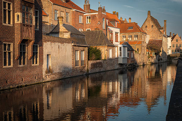 The serene canals of Bruges mirror the city's stunning historic architecture during the golden hour. A breathtaking spring evening in the heart of the old town, bathed in warm sunset hues
