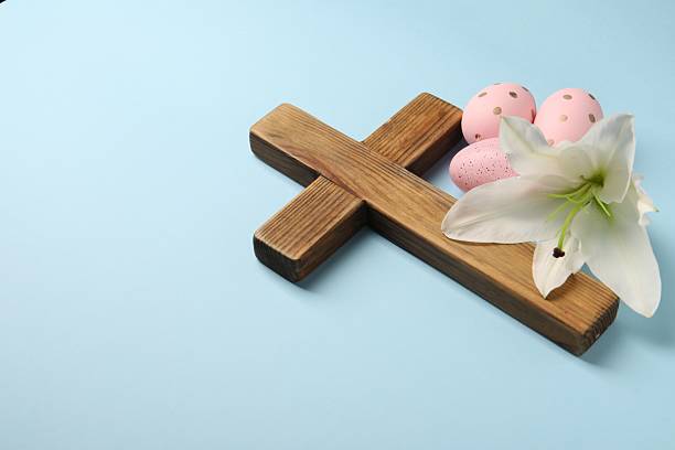 istock Wooden cross, painted Easter eggs and lily flower on light blue background, space for text 2206929790