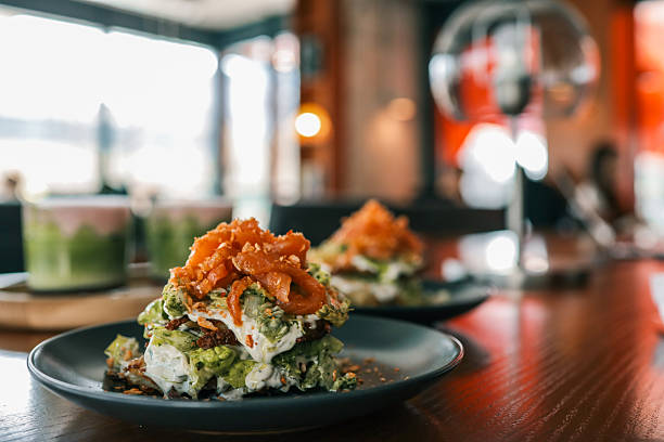 istock Close-up of a gourmet salad stack with creamy dressing and caramelized onions, served on a dark plate in a cozy modern cafÃ© setting with blurred background 2206931418