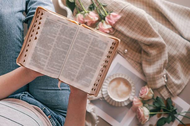 Person reading the Bible while relaxing with coffee and flowers. A cozy moment with soft lighting, delicate pink roses, and a warm, peaceful atmosphere