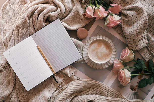 pose à plat d’un agenda hebdomadaire ouvert avec un stylo, une tasse à café, des roses roses et des tissus neutres douillets. idéal pour la planification, la tenue d’un journal ou les thèmes de style de vie productifs avec une esthétique féminin - journal intime cocooning photos et images de collection