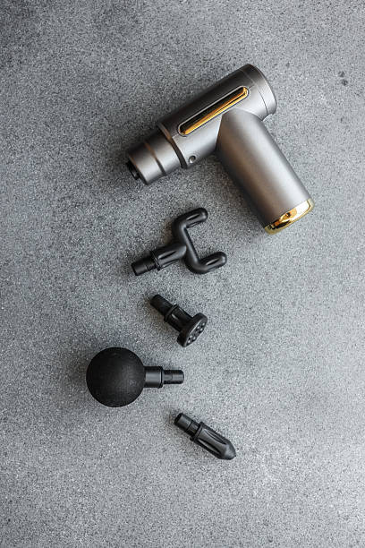 istock Modern massage gun with four interchangeable heads displayed on a grey textured surface, showcasing sleek design and multiple functionality options for muscle therapy 2206934337