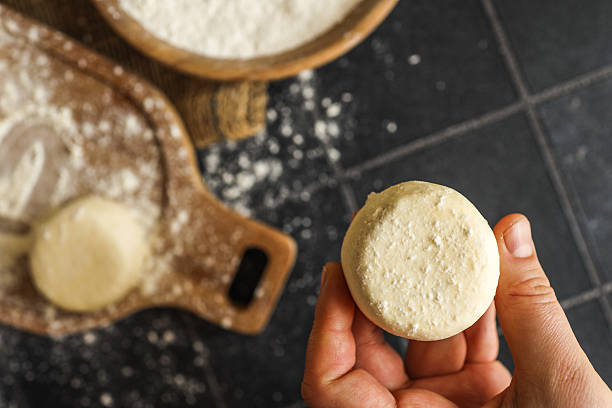 istock Close-up of a hand holding a raw dough round over a floured kitchen counter with baking tools in the background 2206936931