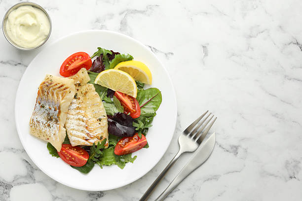 istock Tasty cod cooked served with salad on white marble table, flat lay. Space for text 2206937887